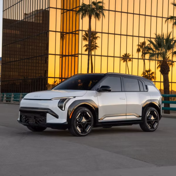 Электромобиль Kia EV3 2027 на дороге у зданий с панелями из стекла и пальмами