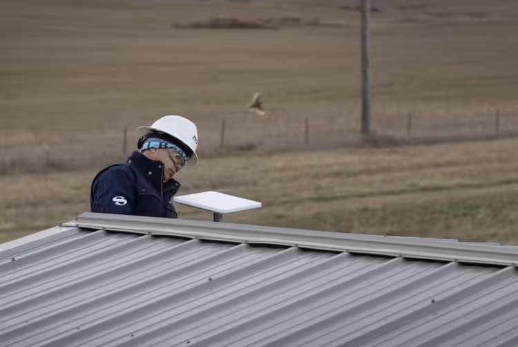 Человек в каске и наушниках с ноутбуком на крыше здания