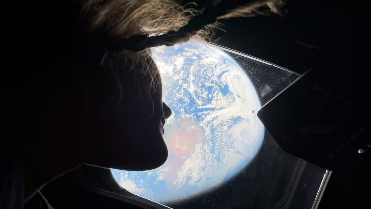 Голова женщины внутри космического корабля Artemis II смотрит в окно на Землю