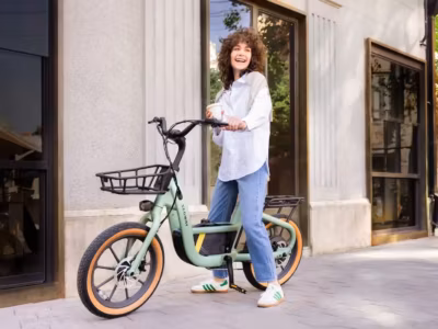 Женщина с кудрявыми волосами и белой рубашкой рядом с электровелосипедом Segway Muxi на улице