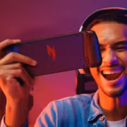 Молодой человек держит смартфон Acer Nitro Blaze Link с игровой клавиатурой и мышью у ноутбука