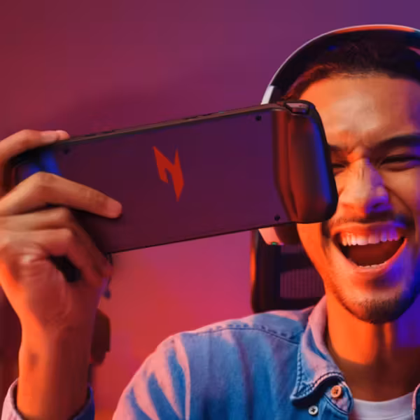 Молодой человек держит смартфон Acer Nitro Blaze Link с игровой клавиатурой и мышью у ноутбука