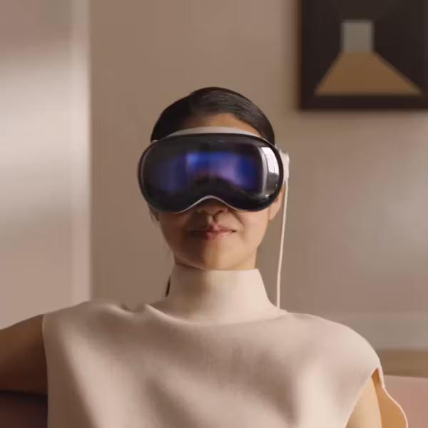 Женщина с очками виртуальной реальности Apple Vision Pro сидит на диване