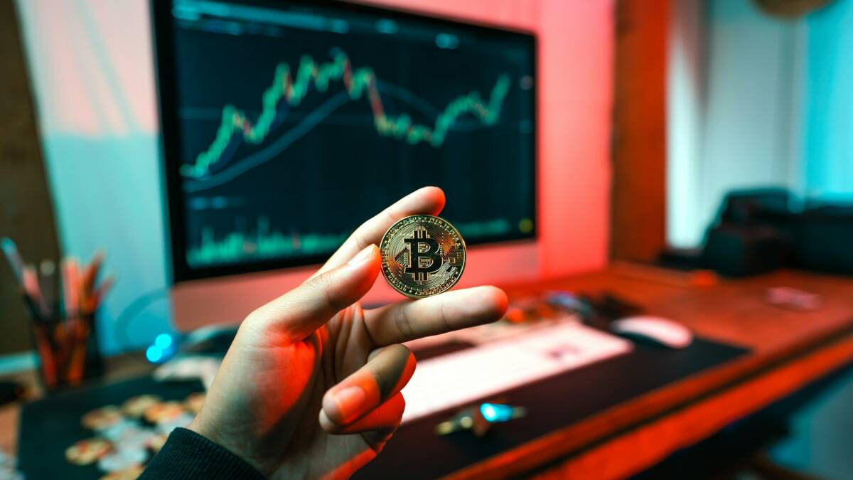 Биткойн Bitcoin в руке у человека на фоне монитора с графиком