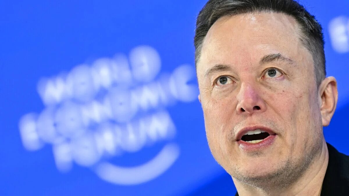 Мужчина говорящий перед синей стеной с логотипом SpaceX