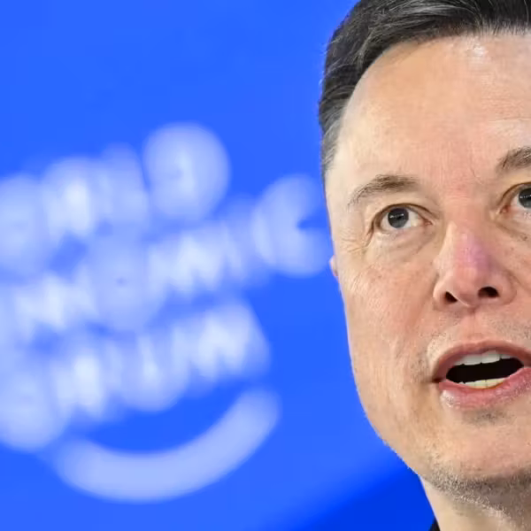 Мужчина говорящий перед синей стеной с логотипом SpaceX