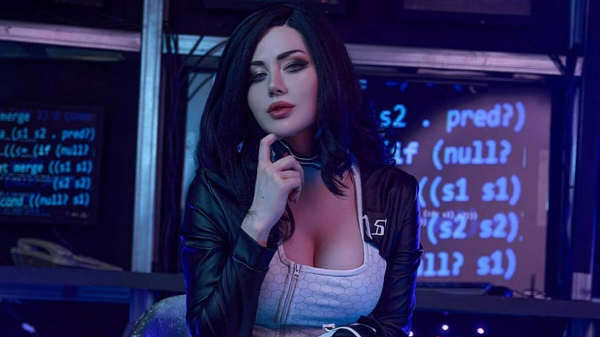 Косплей Миранды Лоусон из Mass Effect 2 девушка с чёрными волосами в черной кожаной куртке и белом топе на фоне компьютерных экранов