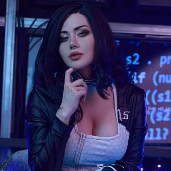 Косплей Миранды Лоусон из Mass Effect 2 девушка с чёрными волосами в черной кожаной куртке и белом топе на фоне компьютерных экранов
