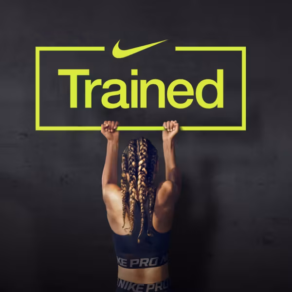 Тренирующаяся женщина держит рамку с надписью Trained на фоне черной стены