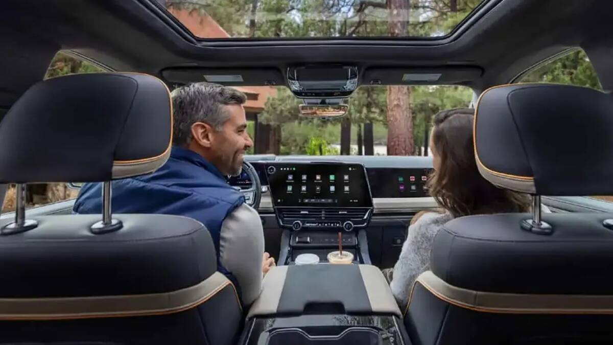 Внутри электромобиля GM Chevrolet Silverado и GMC Sierra 2027 автомобиля показывают сенсорный экран и два человека разговаривают